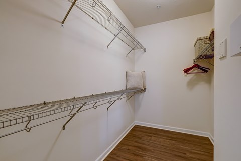 A walk in closet with a white wall and a wooden floor.