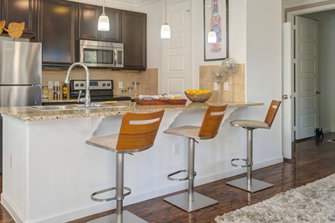 A kitchen with a white counter top and brown bar stools.