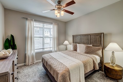 A bedroom with a large bed, a ceiling fan, and a window with curtains.