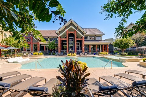 A pool area with sun loungers and a building in the background.