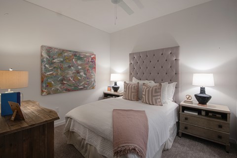 A bedroom with a large bed, a wooden nightstand, and a painting on the wall.