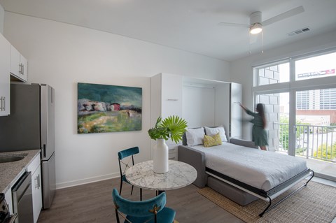 A bedroom with a bed, a table, a chair, and a painting on the wall.