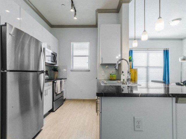A kitchen with a stainless steel refrigerator and a black countertop.