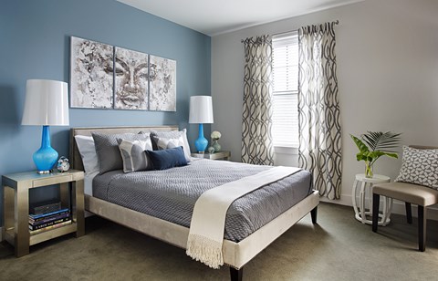 A bedroom with a bed, two lamps, a painting, and a plant.