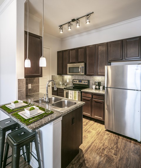 A kitchen with a stainless steel refrigerator and dark brown cabinets.