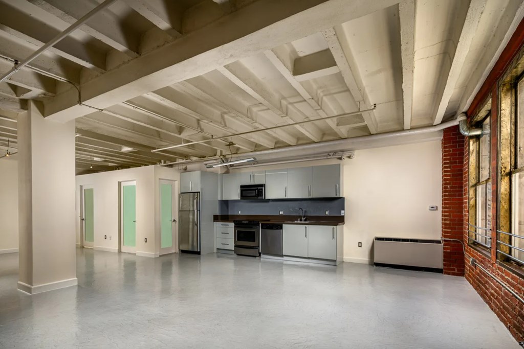 A large empty room with a kitchen area in the back.