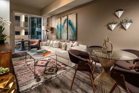 A living room with a white sofa, a glass coffee table, and a large abstract painting on the wall.