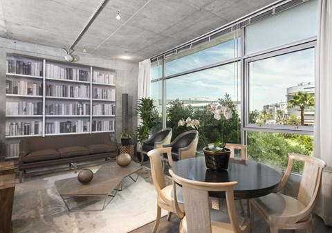 A modern living room with a glass table and chairs, a sofa, and a bookshelf.