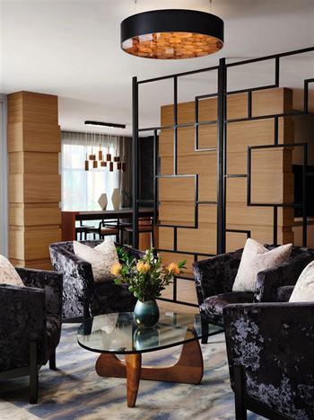 A modern living room with a glass coffee table and dark velvet chairs.