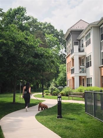 A woman walking her dog on a path in front of a building.