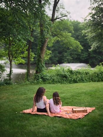 Two girls sitting on a blanket in a park.