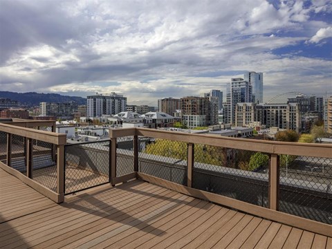 A wooden deck overlooks a cityscape with buildings and a cloudy sky.