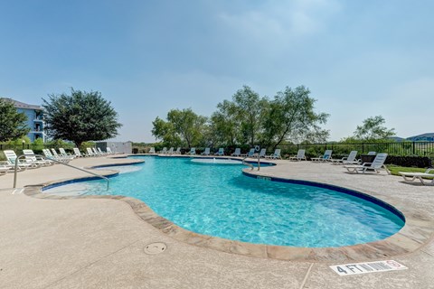 A large outdoor swimming pool with lounge chairs and a clear blue sky.