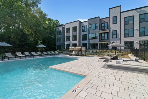 A swimming pool surrounded by a brick patio and lounge chairs.
