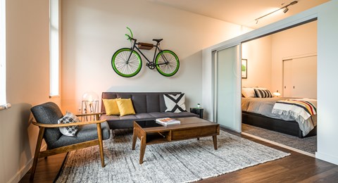 A living room with a grey couch, a wooden coffee table, and a bicycle decoration on the wall.