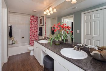 Master bathroom with floating vanities, quartz countertops, backlit vanity mirror, walk-in shower with Euro shower door and quartz-topped bench seat at The Plaza Museum District, Houston, TX, 77004