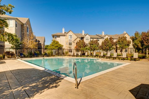 A swimming pool surrounded by a tiled patio and lounge chairs in front of a row of houses.