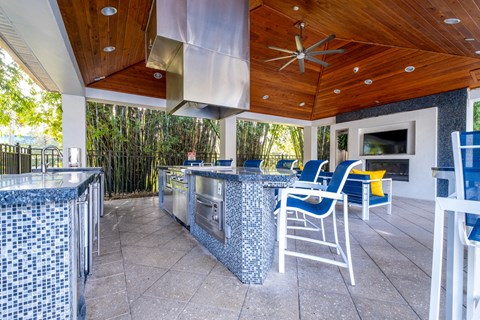 the outdoor kitchen has a grill and bar with blue chairs