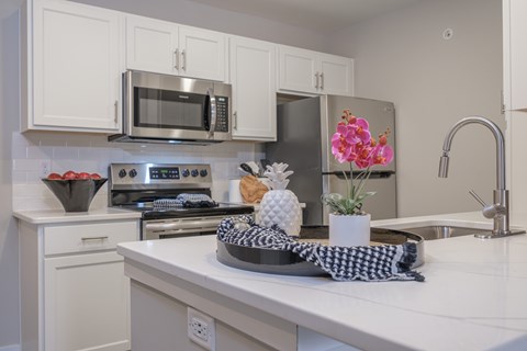 A kitchen with white cabinets and a checkered cloth on the counter.