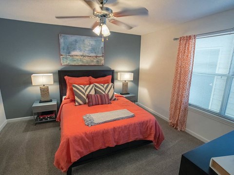 A bedroom with a bed, two lamps, a ceiling fan, and a painting on the wall.
