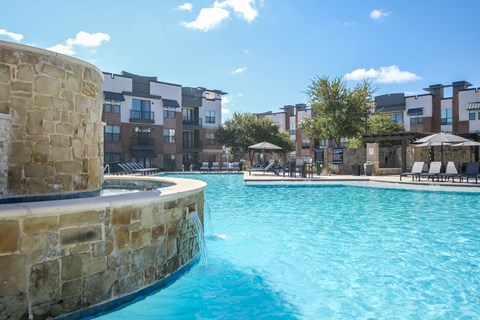 A swimming pool with a stone wall and a building in the background.
