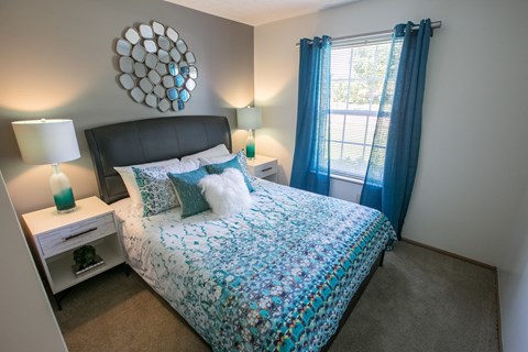 A bedroom with a bed, nightstands, and a window with blue curtains.