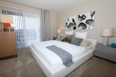 A bedroom with a large bed, a nightstand, and a window with blinds.
