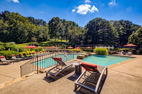 A large outdoor swimming pool surrounded by trees and lounge chairs.