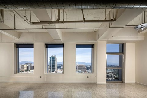 A large empty room with three windows overlooking a cityscape.