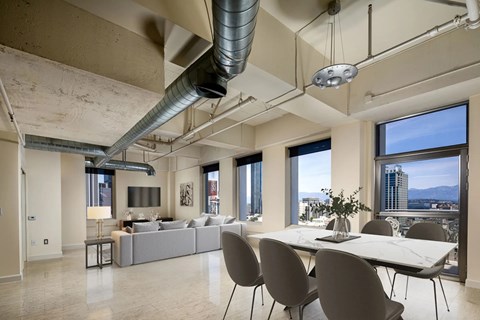 A modern living room with a grey couch and a white dining table.