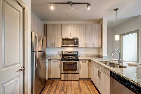A kitchen with a stainless steel refrigerator and oven, wooden cabinets, and a marble countertop.