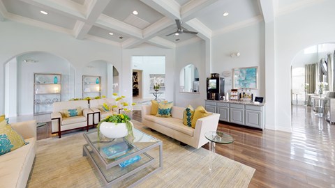 A spacious living room with a glass coffee table and a white sofa with yellow pillows.