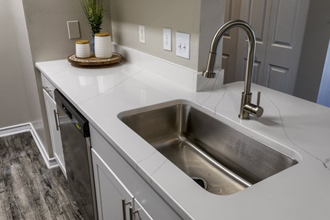 A modern kitchen with a stainless steel sink and white countertop.