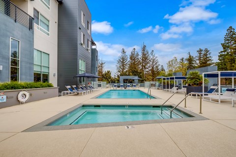 A swimming pool in front of a modern building with trees in the background.