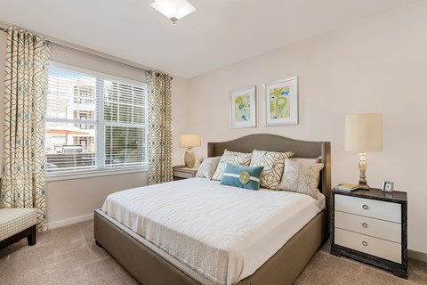A bedroom with a large bed, a nightstand, and a window with curtains.