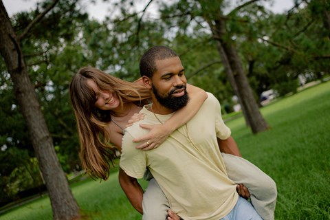 A man is carrying a woman on his back in a park.