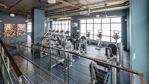 a gym with cardio machines and large windows at Reveal Hackensack apartments