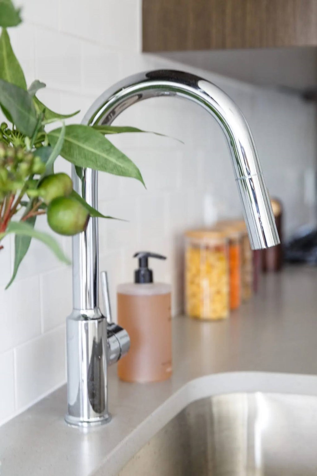 A kitchen sink with a silver faucet and a vase of greenery on the counter.