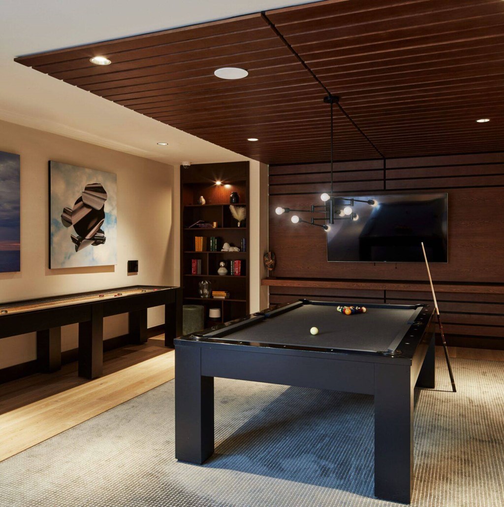 A pool table with a green ball and a cue stick in a room with a wooden ceiling and a bookshelf.