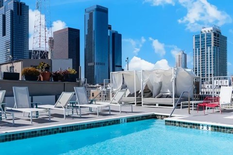 A pool with chairs and umbrellas on a rooftop with a city skyline in the background.