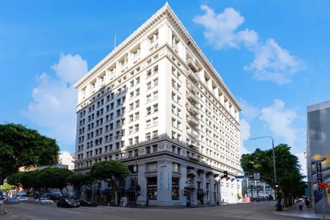 A large white building with a pointed top is surrounded by trees and cars on the street.