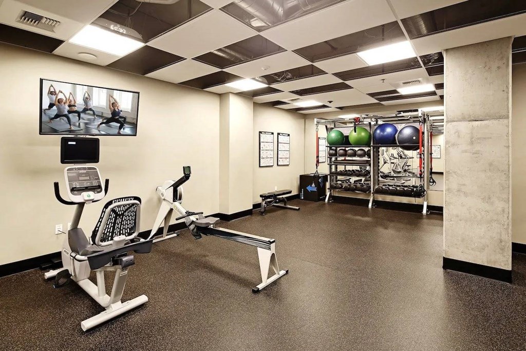 A gym with a rowing machine, a bench press, and a television.