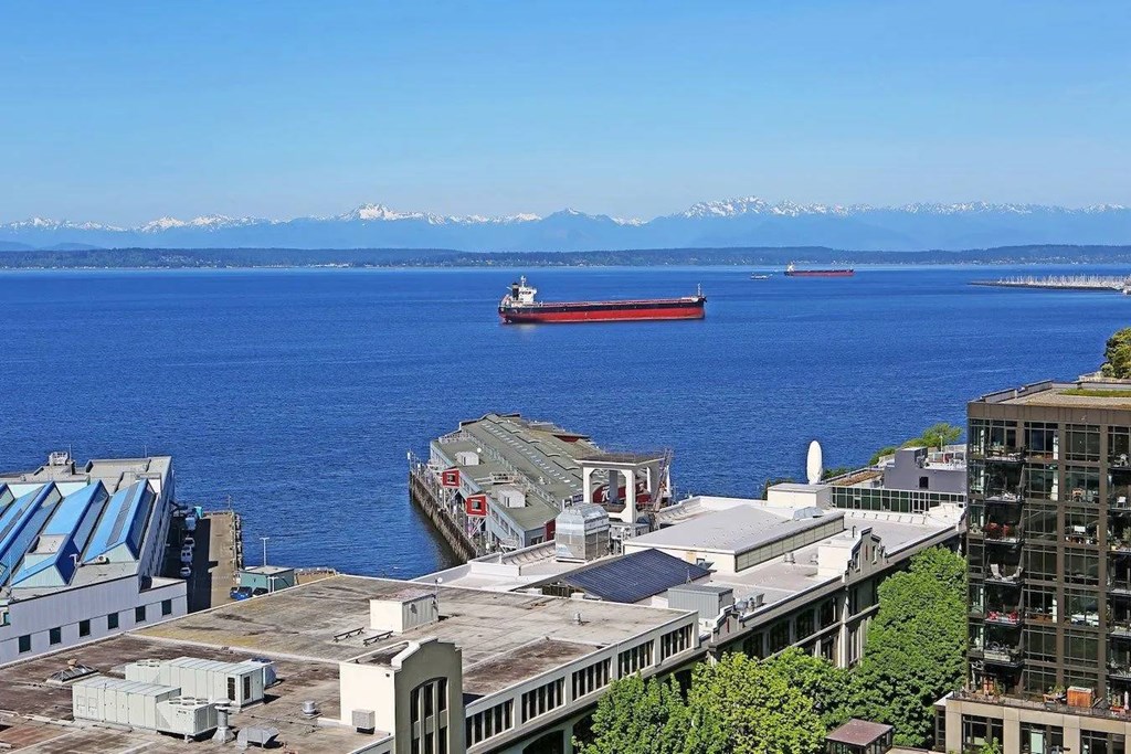A large ship is docked at a port with a mountain range in the distance.