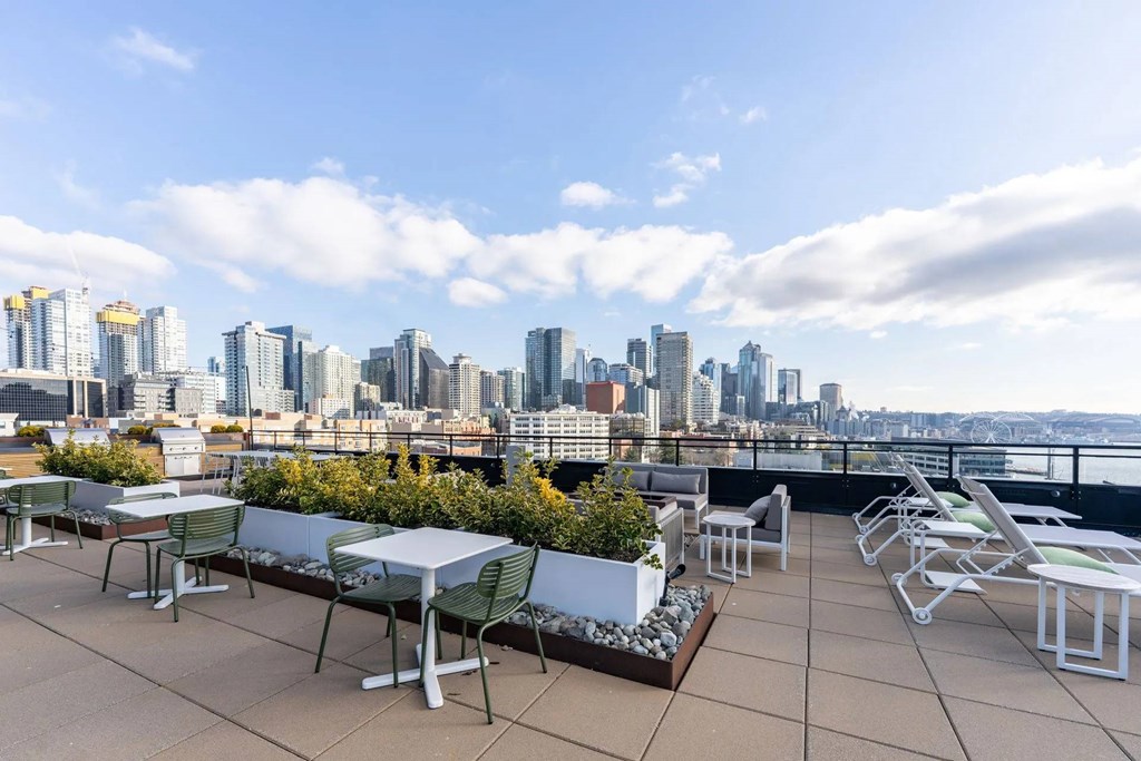A rooftop patio with tables and chairs overlooking a city skyline.
