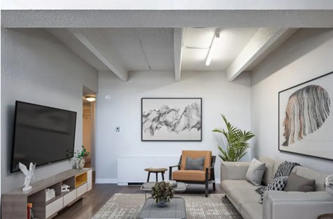 A living room with a grey couch, a black television, and a large abstract painting on the wall.