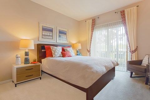 A bedroom with a large bed, a nightstand with two lamps, and a chair.