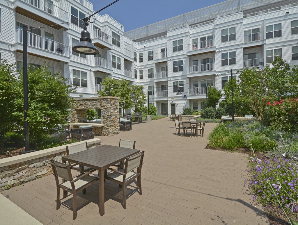 Outdoor patio with fireplace and dining tables with chairs surrounded by lush landscaping