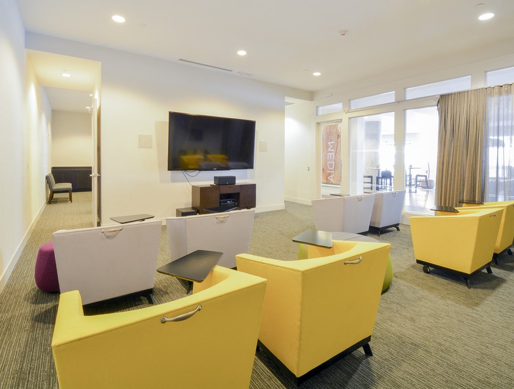 Resident lounge space with bright yellow chairs facing wall-mounted TV