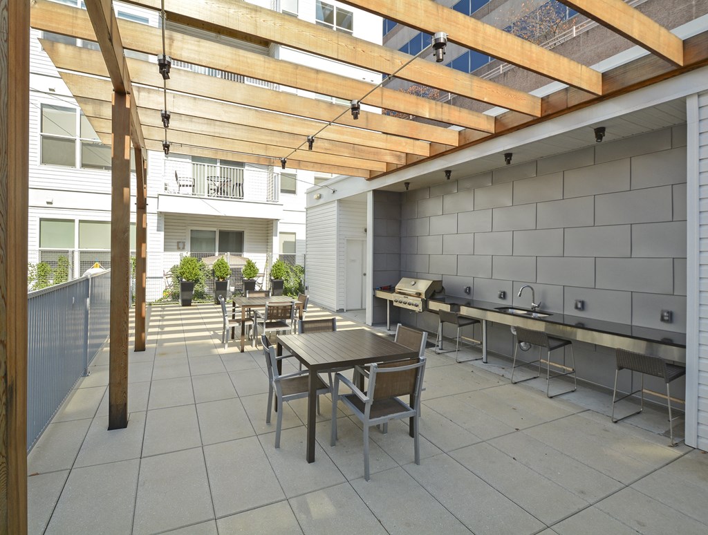 Outdoor grill station with dining tables and chairs under trellis