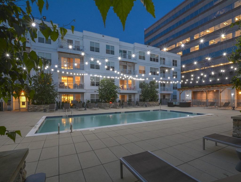 Night view of pool with overhead string lights and lounge chairs surrounding pool
